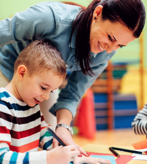 A woman helping a child with crafts in a classroom.