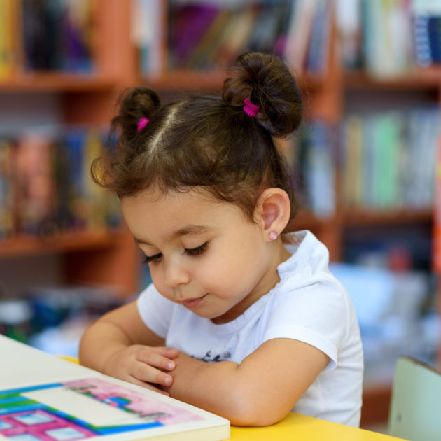 A little girl reading a book in a library.