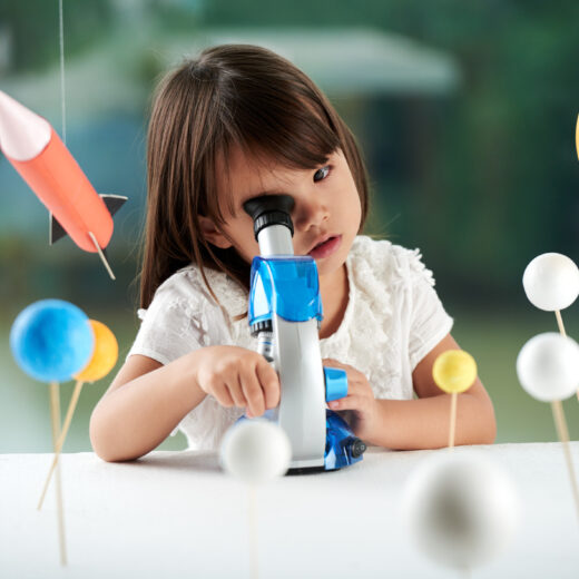 A little girl looking through a telescope.
