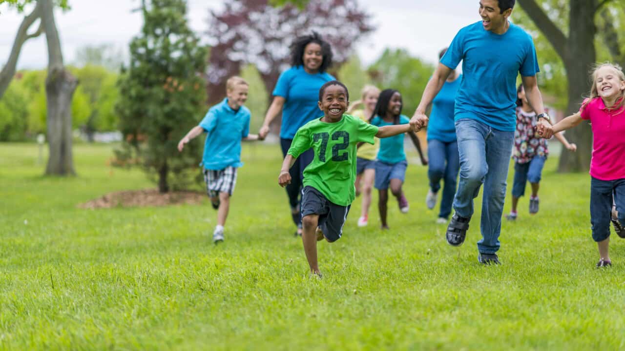 A group of children and adults running across a grassy park.